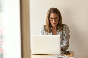 Frau mit Brille sitzt in Businesskleidung an einem Laptop.